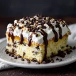 Slice of cannoli poke cake with creamy white filling, chocolate chips, caramel drizzle, and powdered sugar on white plate