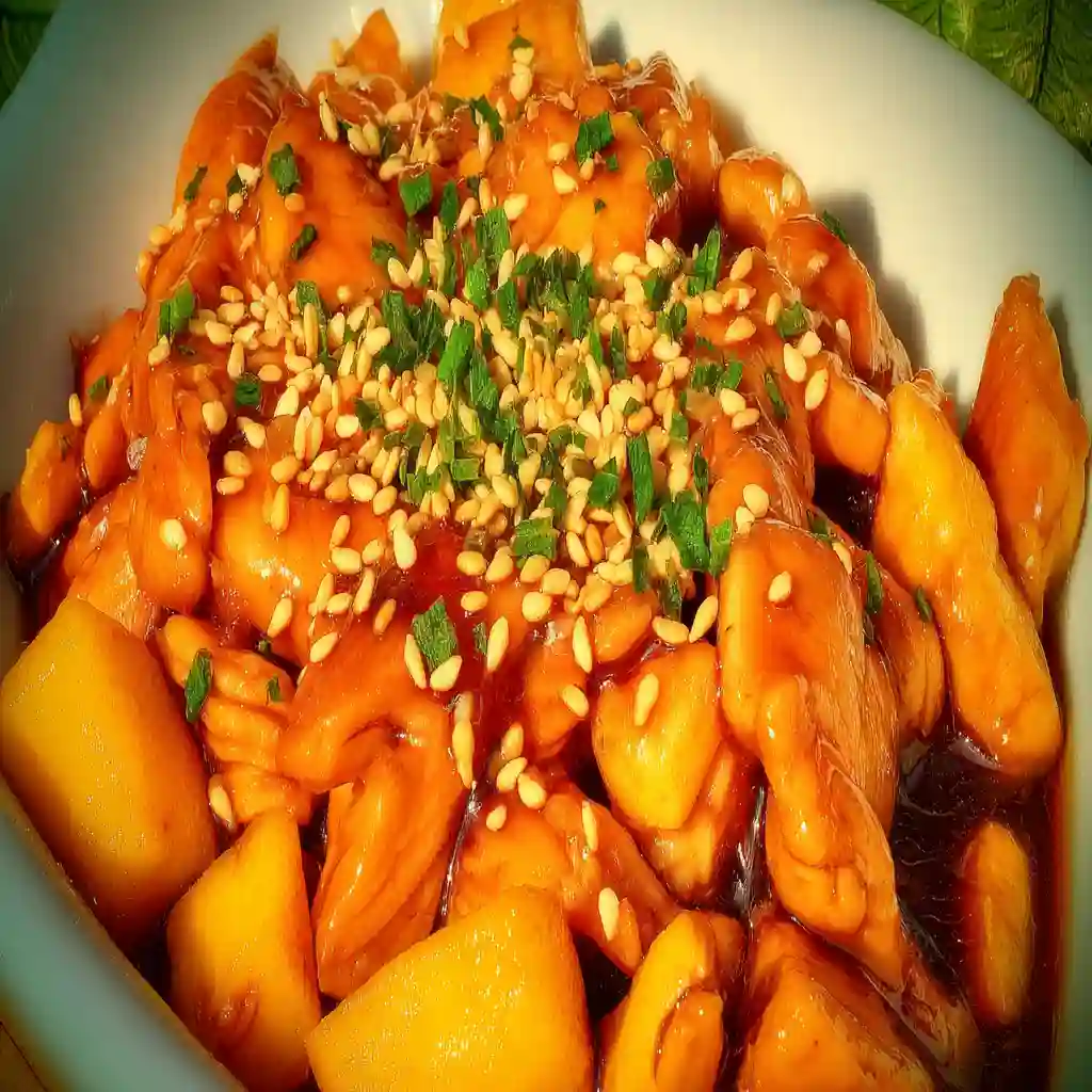 Crock Pot Marry Me Chicken 2 Orange chicken served in a bowl, coated with a glossy orange glaze and sprinkled with sesame seeds and chopped green onions.