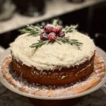 A beautifully decorated rustic Christmas themed cake with snowy coconut, sugared cranberries, and fresh rosemary on a wooden stand.