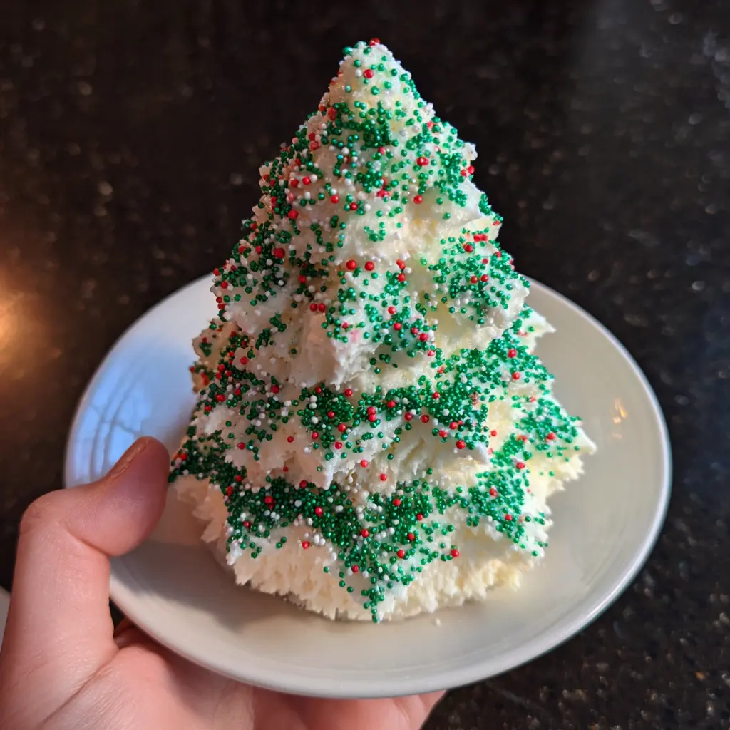 Copycat Little Debbie Christmas Tree Cake Recipe 2 Delicious white frosted Christmas tree cake with green, red, and white sprinkles, held on a white plate.