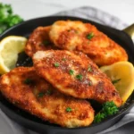 “Golden brown crispy baked breaded chicken breasts on a parchment-lined baking sheet, garnished with fresh parsley.”