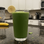 A vibrant green spinach banana smoothie in a tall glass, garnished with a fresh mint leaf, ready to enjoy.